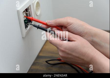 female hands use the probes of a digital multimeter to check the current voltage in an electrical outlet. Stock Photo