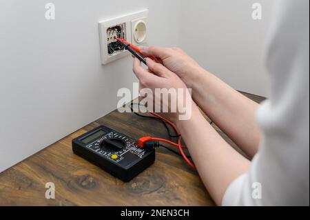 woman using digital multimeter to check current voltage in electric socket. Stock Photo