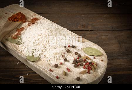 Rice in a jute bag with a wooden spoon on the kitchen table. Nearby on a cutting board bay leaf and different types of pepper Stock Photo