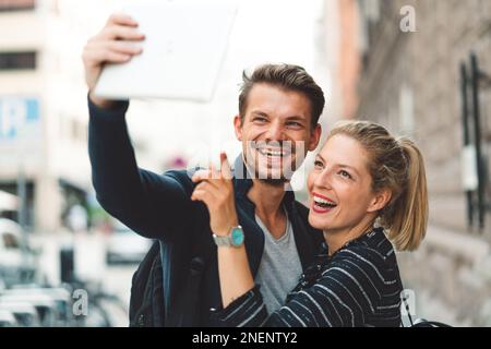 Happy caucasian couple taking selfies in the city on a sunny day Stock Photo
