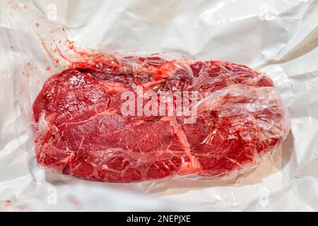 Uncooked raw red sirloin or ribeye steak cut macro closeup of texture wrapped in paper plastic wrap packaging from butcher Stock Photo
