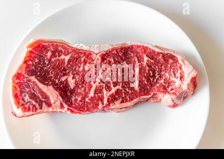 Flat top view of raw red strip or ribeye steak cut closeup of texture butcher cut on white plate and background Stock Photo