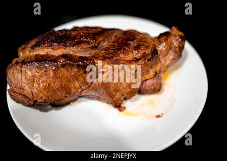 Macro closeup of cooked ribeye, strip or sirloin steak with thick cut and brown crust on white plate and background resting with juices Stock Photo
