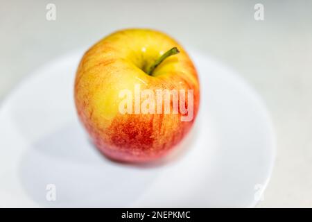 One washed striped yellow red gala or fuji apple macro closeup of texture on white plate studio shot on table with colorful skin variety Stock Photo