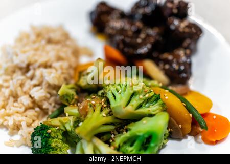 Cooked green broccoli stir-fry vegetables macro closeup on white dinner healthy plate with meat pieces of beef heart sprinkled in sesame seeds and bro Stock Photo