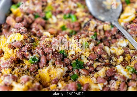 Macro closeup of beans with fried bacon and scrambled eggs as feijao tropeiro Brazilian dish and serving spoon in buffet tray for catered event Stock Photo