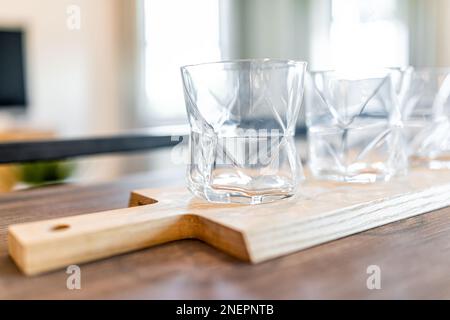 Glasses on kitchen table wooden cutting board tray at interior staging model home house macro closeup with living room in background Stock Photo