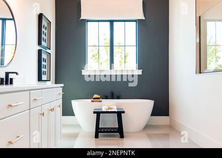 Bathtub in bathroom staging model home house or hotel with modern luxury white cabinets interior, window with light and mirrors Stock Photo