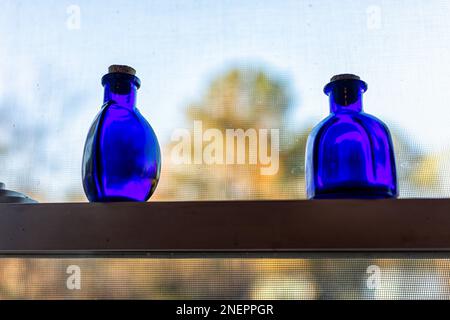 Kitchen window blue medicine herbal elixir bottle decorations decor with empty glass in sunlight closeup on shelf with cozy atmoshpere Stock Photo