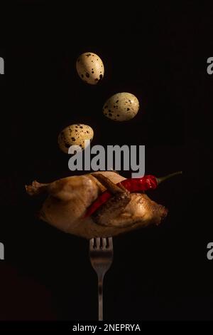 Quail fork eggs. Fried quail on a fork close-up on a black background serhu three quail eggs fly under the wing of a red hot pepper pod. vertical Stock Photo