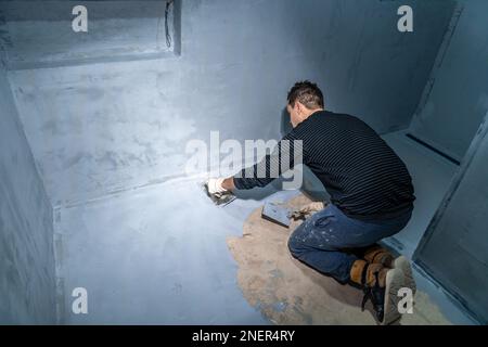 man applies insulation to a bathroom floor Stock Photo