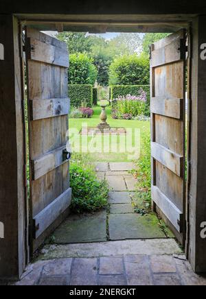 A view through an old wooden doorway at Wollerton Old Hall Gardens garden Wollerton Market Drayton Shropshire England UK Stock Photo