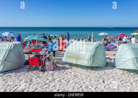 Naples, USA - December 28, 2021: Vanderbilt beach in Florida southwest with many people by tents and white sand on sunny winter day and blue sky Stock Photo