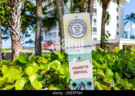 Naples, USA - March 30, 2022: Collier County, Florida gulf of mexico coast with beach access on sunny day and sign for city of Naples cigarette dispos Stock Photo