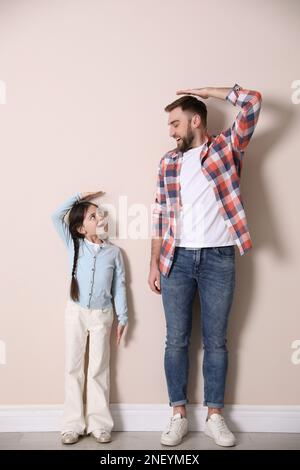 Father and daughter comparing their heights near beige wall indoors Stock Photo