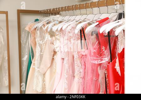 Different beautiful dresses on hangers in rental clothing salon Stock Photo
