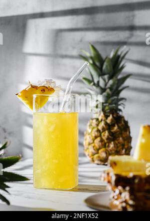 pineapple juice on a gray background.there is a pineapple and pineapple slices nearby, sunlight Stock Photo