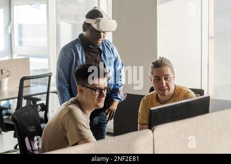 IT Development Team Working on VR Project. Black man wearing VR headset. Virtual world. Diverse men programmers using VR technologies and computer to Stock Photo