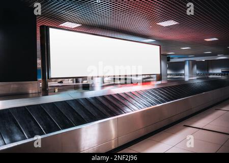 Shot in low-key of a very large rectangular blank billboard mockup facing a baggage claim in an airport terminal; a big white blank advertisement temp Stock Photo