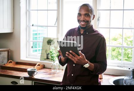 Im connected to the office even when Im at home. Portrait of a handsome young businessman using a digital tablet while working from home during the Stock Photo
