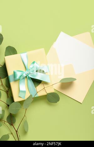 Envelope with blank card, gift box and eucalyptus branches on green background. Hello spring Stock Photo