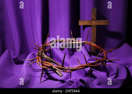 Cross with purple fabric, nails and crown of thorns on beige background ...