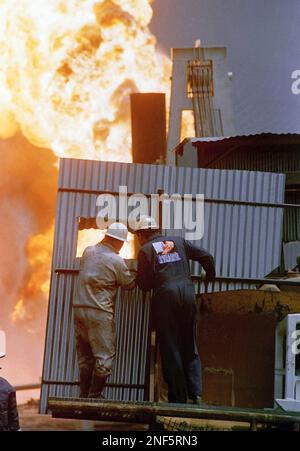 Boots Hansen (left) and John Carpenter of Boots & Coots Co. are shielded from the heat as they ride a massive crane like rig used in an attempt to snuff out a burning oil well, Saturday, March 30, 1991 in Kuwait. The attempt failed due to low water pressure at the site. (AP Photo/David Longstreath)