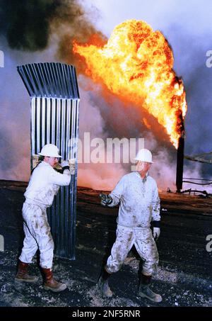 Boots Hansen, right, of Boots & Coots Co. is shielded from the heat of a burning oil well, Saturday, March 30, 1991 in the Greater Burgan Oil Fields in Kuwait. Hansen tried to extinguish the fire by 'collaring' the flame with a massive 15 foot vertical cylinder and dousing it with water but failed because of low water pressure. (AP Photo/Greg Gibson)