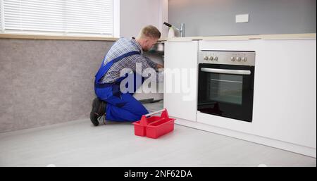 Plumber Cleaning Drain And Pipe In Kitchen Stock Photo
