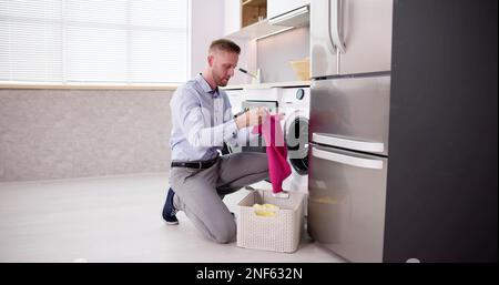 Young Man Loading Clothes Into Washing Machine In Kitchen Stock Photo