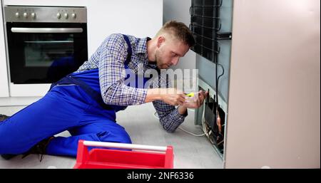 Cropped Image Of Serviceman Working On Fridge With Screwdriver At Home Stock Photo