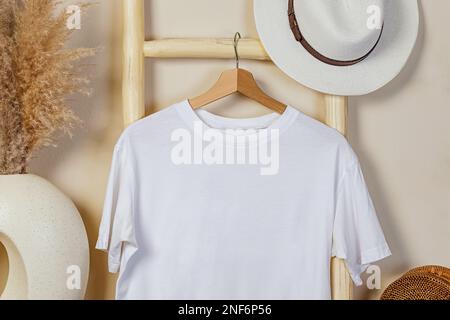 White cotton t-shirt on the wooden hanger. Mock-up in boho interior. Stock Photo