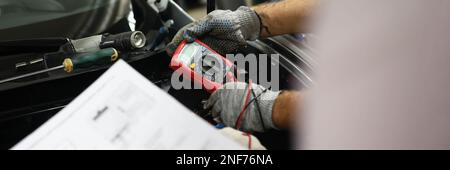 Mechanical service using multimeter to check voltage level in car battery and auto documentation diagram Stock Photo