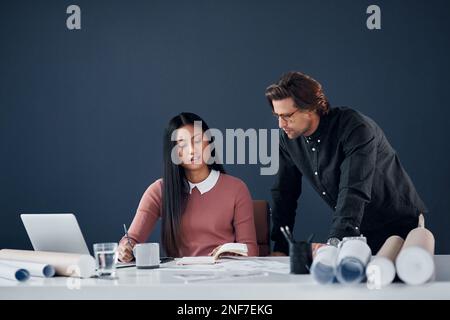 Theres a few things we need to go over today. two young architects going over building plans and paperwork together in their office. Stock Photo
