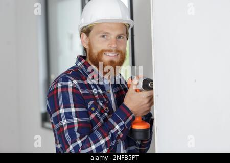 builder drilling a hole in a new white wall Stock Photo