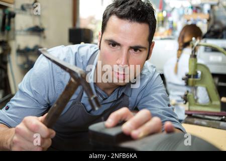 cobbler in uniform holding hammer and shoe workpiece Stock Photo