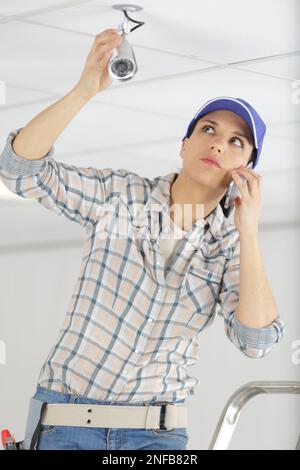 worried female technician using the phone while installing camera Stock Photo
