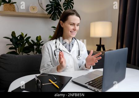 Smiling female doctor physician wearing white uniform and stethoscope using laptop computer at workplace. Positive woman professional medic consulting Stock Photo
