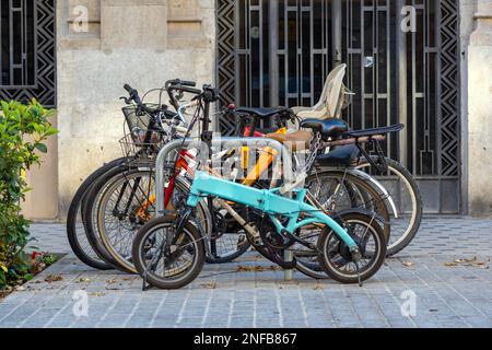 Set of different bicycles parked with chains and padlocks on the sidewalk in a street in Barcelona. A bicycle is blue and foldable. Stock Photo