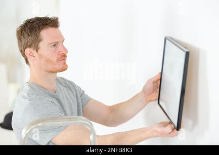 repairman putting picture frame onto wall Stock Photo