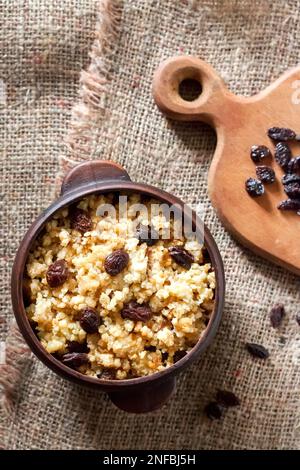 Sweet millet porridge with dark raisins in ceramic rustic bowl with walnuts on background Stock Photo