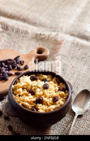 Sweet millet porridge with dark raisins in ceramic rustic bowl with walnuts on background Stock Photo