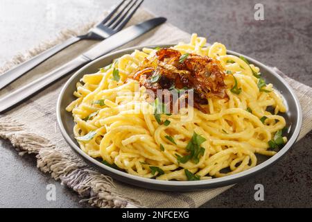 Hot spatzle noodles and grated cheese Emmentaler topped with fried onions closeup on the plate on the table. Horizontal Stock Photo