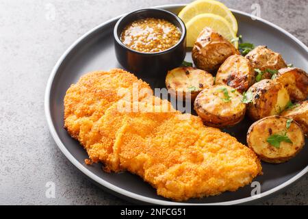 Delicious German Munich schnitzel fried breaded with mustard and horseradish served with baked potatoes close-up in a plate on the table. horizontal Stock Photo