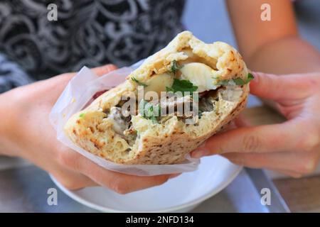 Israeli cuisine. Sabich sandwich (also known as sabih): pita bread filled with eggplants, hard boiled eggs, amba sauce and salad. Stock Photo