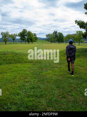 A young man walks toward the Native American Hopewell Culture prehistoric Seip Earthworks burial mound in Ohio. Ancient large long mound. Grass is nea Stock Photo