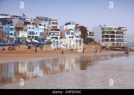 TAGHAZOUT, MOROCCO - FEBRUARY 27, 2022: People visit the beach in Taghazout surfing town near Agadir in Morocco. Stock Photo