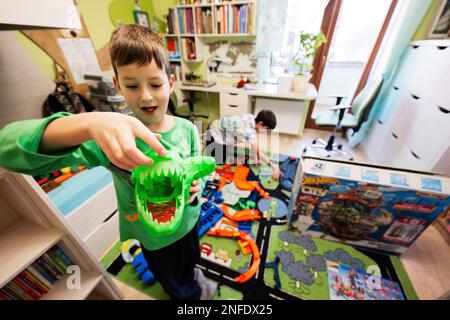 Ternopil, Ukraine - February, 2023: Kids unboxing Hot Wheels City Ultimate Garage, play in children room. Boy hold big green dinosaur. Stock Photo