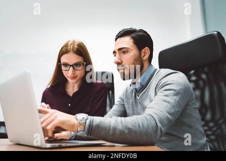Business man and business woman working on a joint project, sitting by the desk looking at the laptop screen Stock Photo