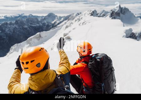 Over the head view, two mountaineers with helmets looking at the view of snowy Alps from high up  Stock Photo